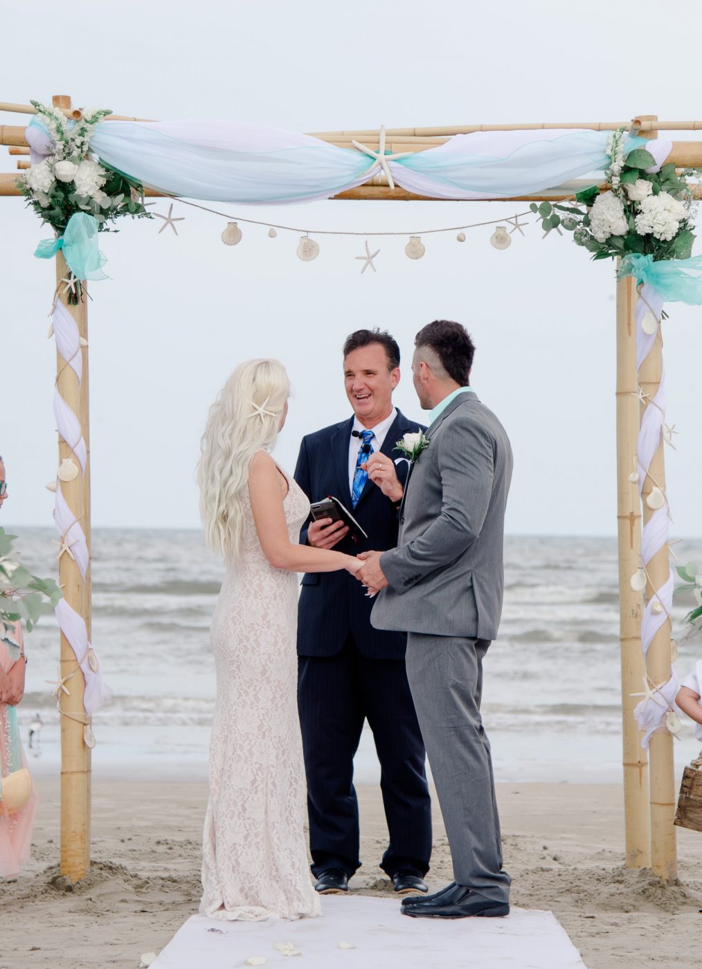reverend john roberts marries couple on the beach under an arch