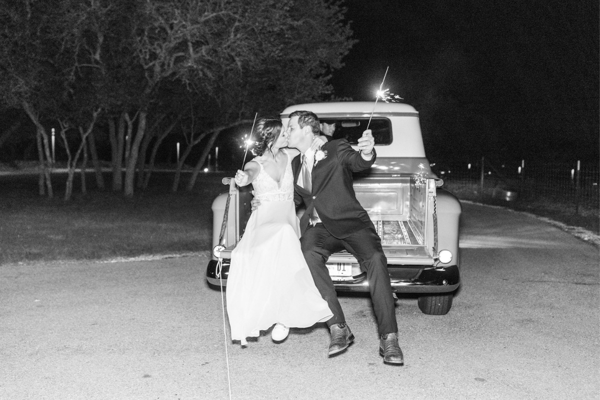 Bride and Groom holding sparklers on the back on a vintage truck while kissing with Texas Wedding Ministers