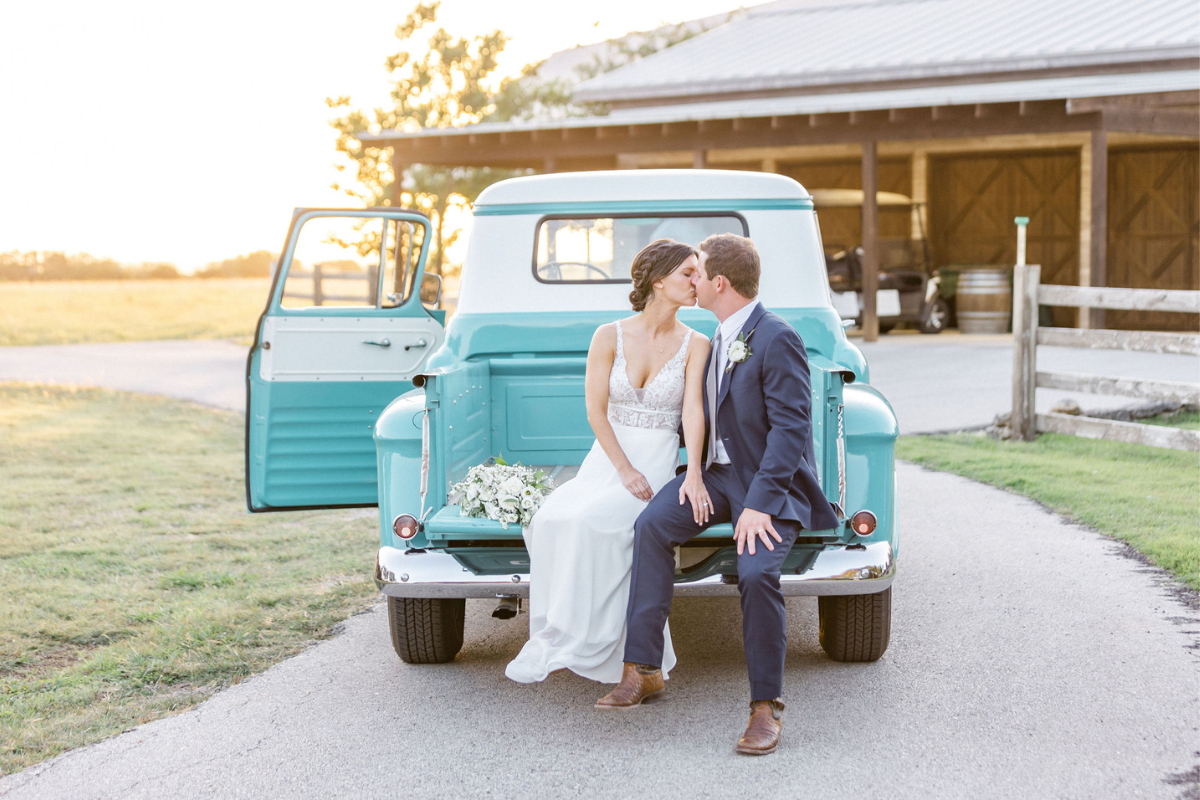 Texas Wedding Ministers couple kissing and sitting on the back on a vintage car at Firefly Farms wedding venue.